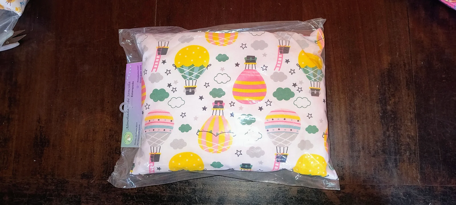 Almohada sencilla estampada con globos de colores, dentro de su empaque.